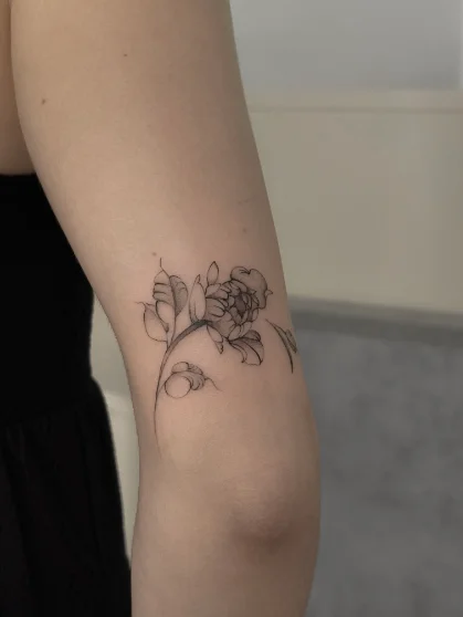 Botaniczny tatuaż fine line piwonii z liśćmi na ramieniu
