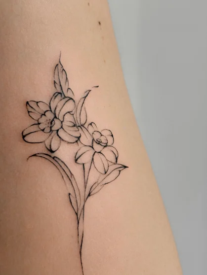 Botaniczny tatuaż fine line gałązki narcyzów na ramieniu